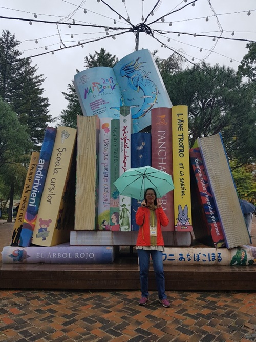 책모양 조형물 앞에서 손으로 브이를 하며 서있는 복지관이용자 사진